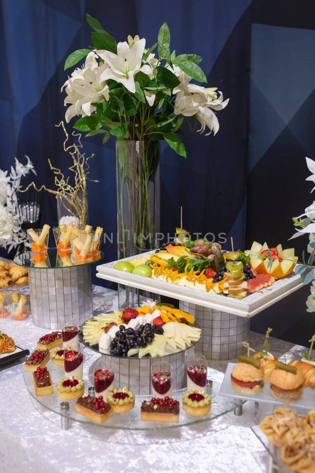 A beautifully adorned catering table with an array of delicious food and drinks. The elegant white floral centerpiece adds sophistication to the display, creating an inviting atmosphere.