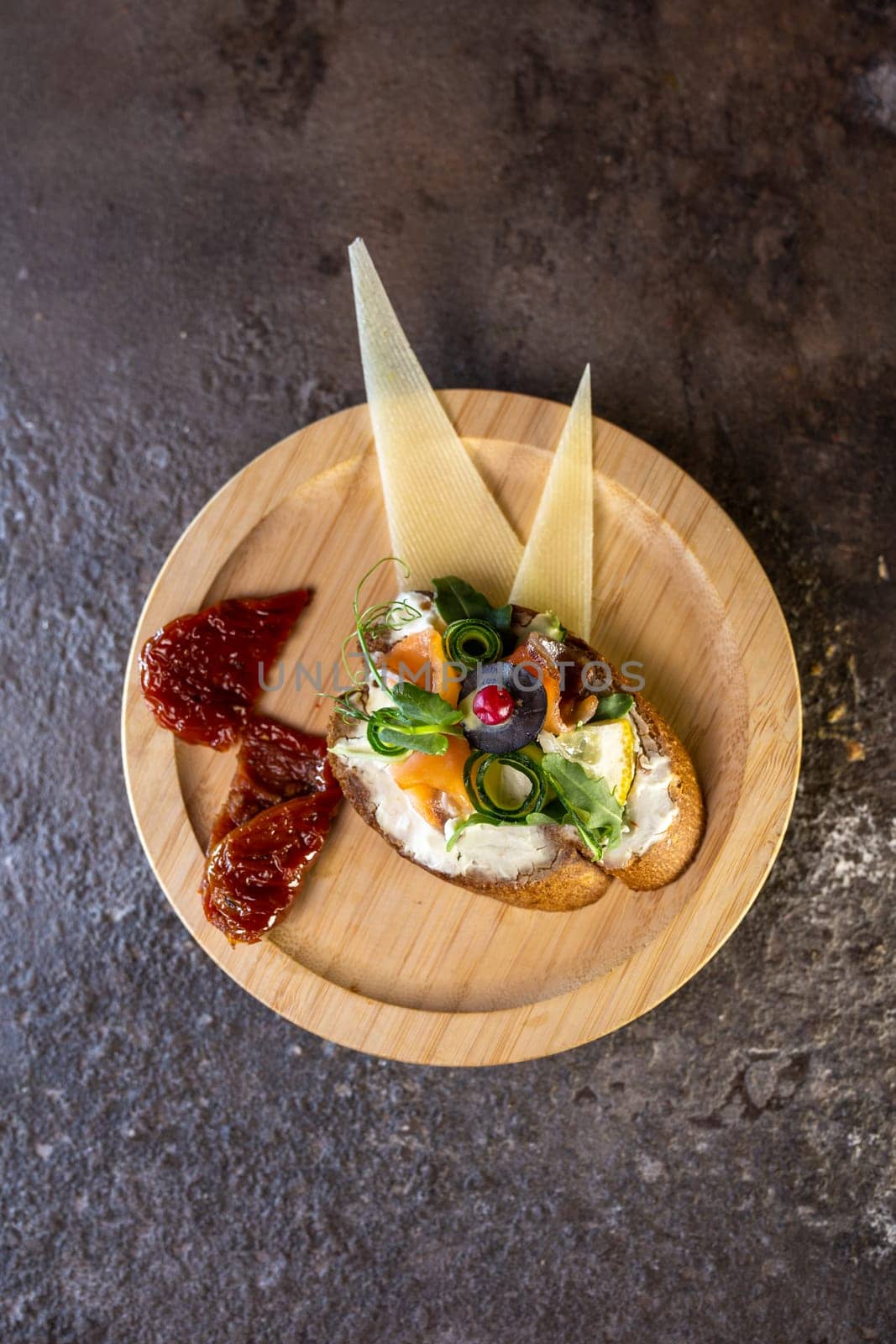 A delicious-looking open-faced sandwich made with cream cheese, cucumber, capers, and herbs on a wooden plate with cheese and sauce on the side. Perfect for a light lunch or snack.