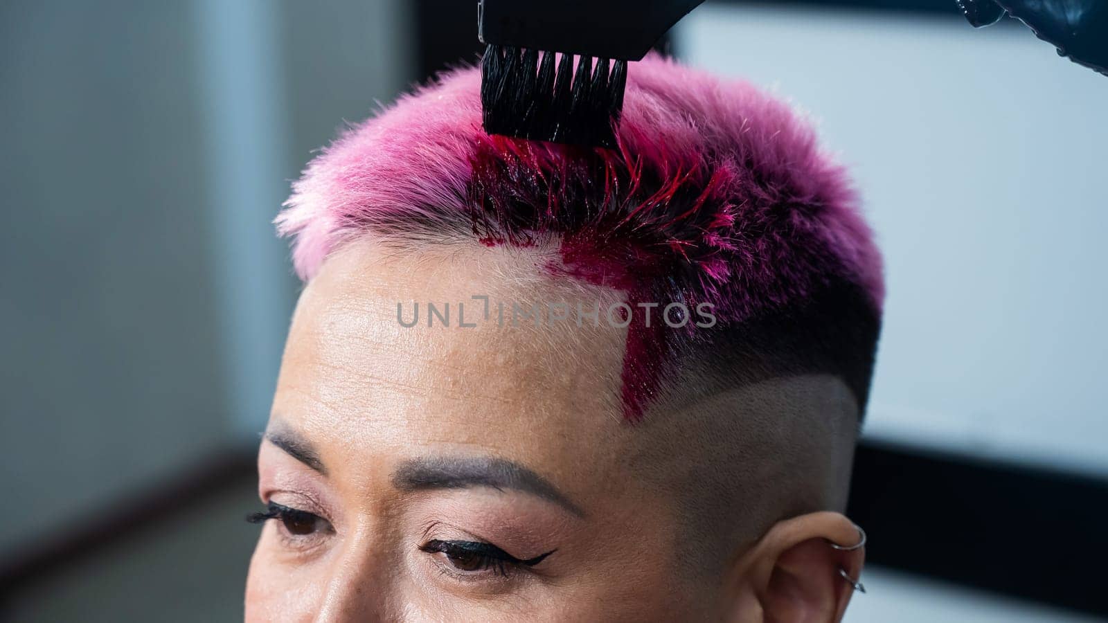 Close-up of the process. The hairdresser dyes the hair of an Asian woman in pink. Short extreme haircut