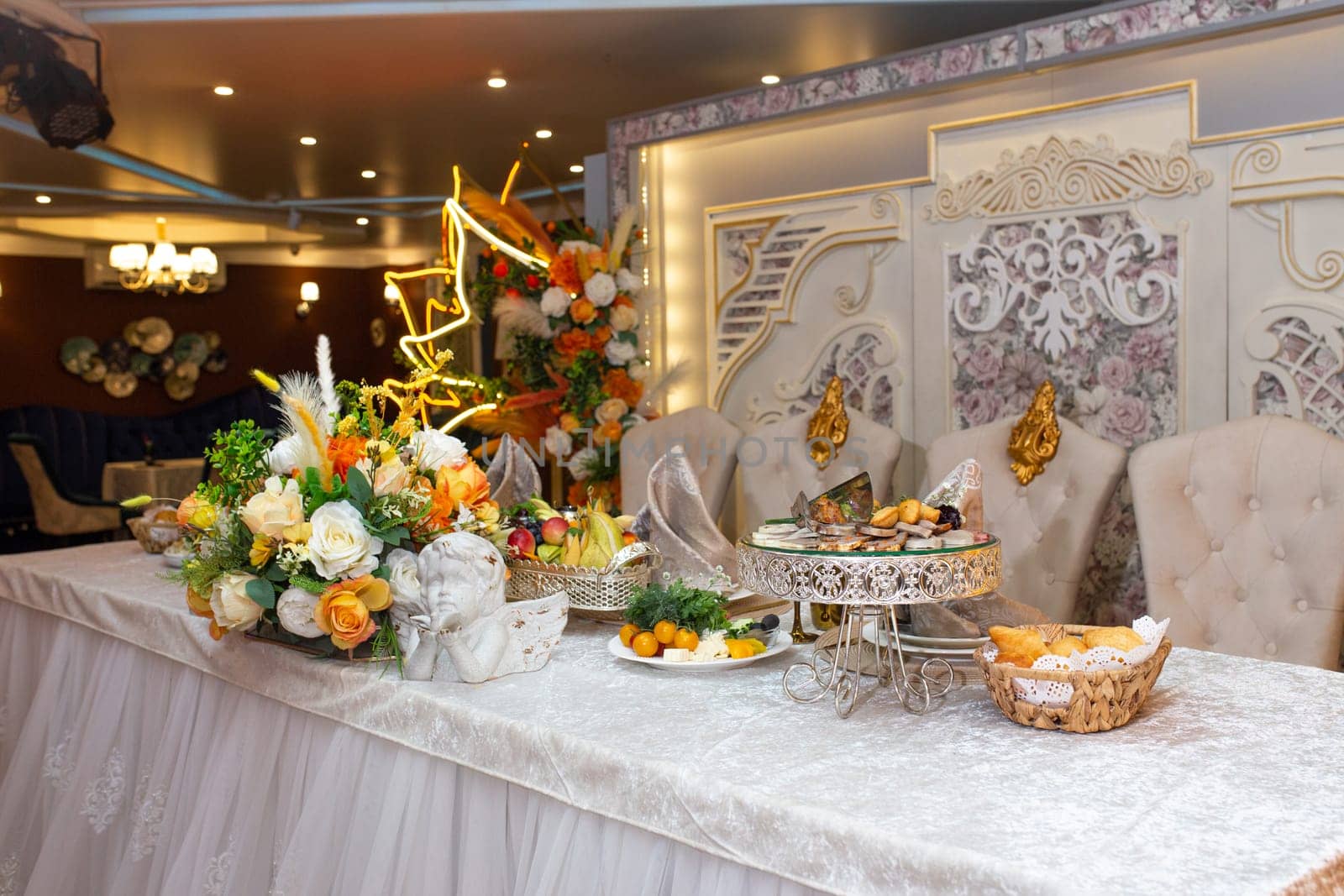 A beautifully decorated wedding table with a centerpiece of flowers and fruit, elegant chairs, and a shimmering chandelier above, creating a magical ambiance for the special occasion.