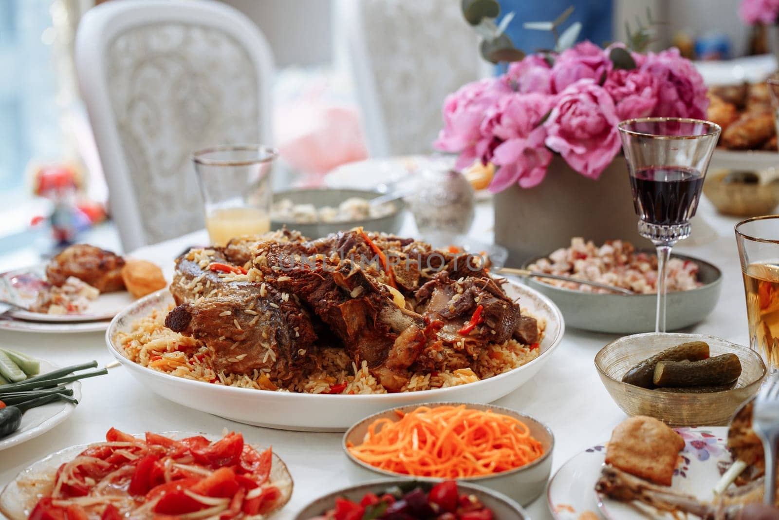 Delicious traditional Uzbek pilaf with tender lamb and fresh vegetables, served with vibrant salads and pickles. Beautifully presented with appetizing colors and a blurred background.