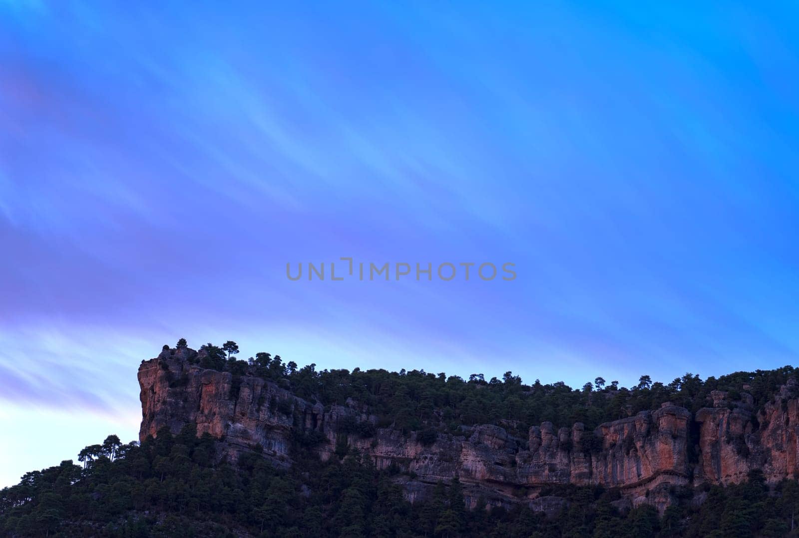 Tranquil landscape featuring a jagged cliff beneath a sky with striking blue and purple streaks.
