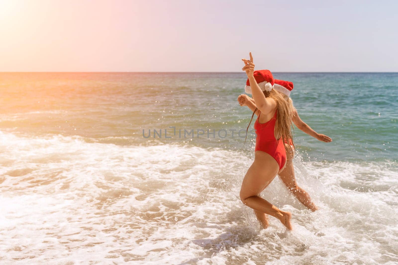 Women in Santa Claus hats run into the sea dressed in red swimsuits. Celebrating the New Year in a hot country by Matiunina