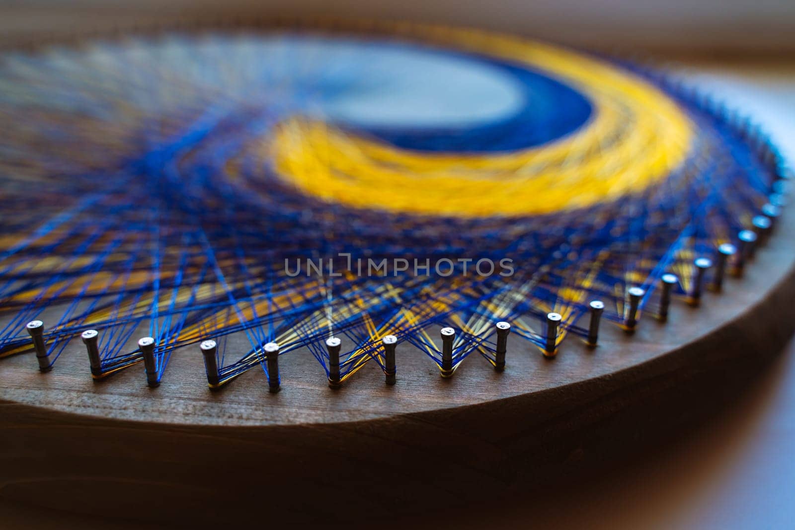 Colored thread mandala on a wooden board with nails. Mandala Moon Harmony Sun esotericism and psychology pictures from yellow and blue silk threads