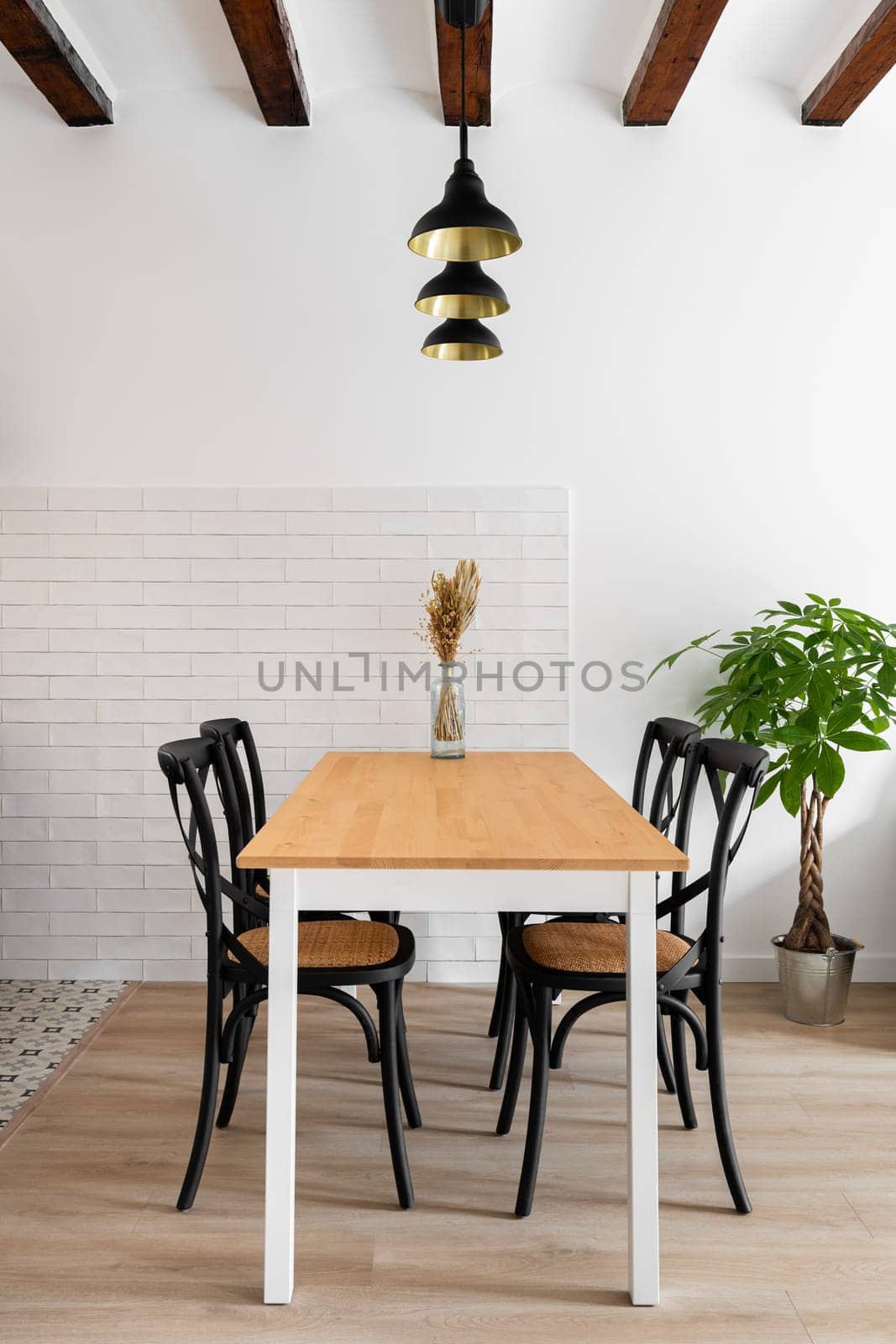 Vertical frame wooden dining table with four designer chairs with lamps and wooden beams on the background of a brick white wall and a plant. Modern kitchen in a new apartment. Copyspace.