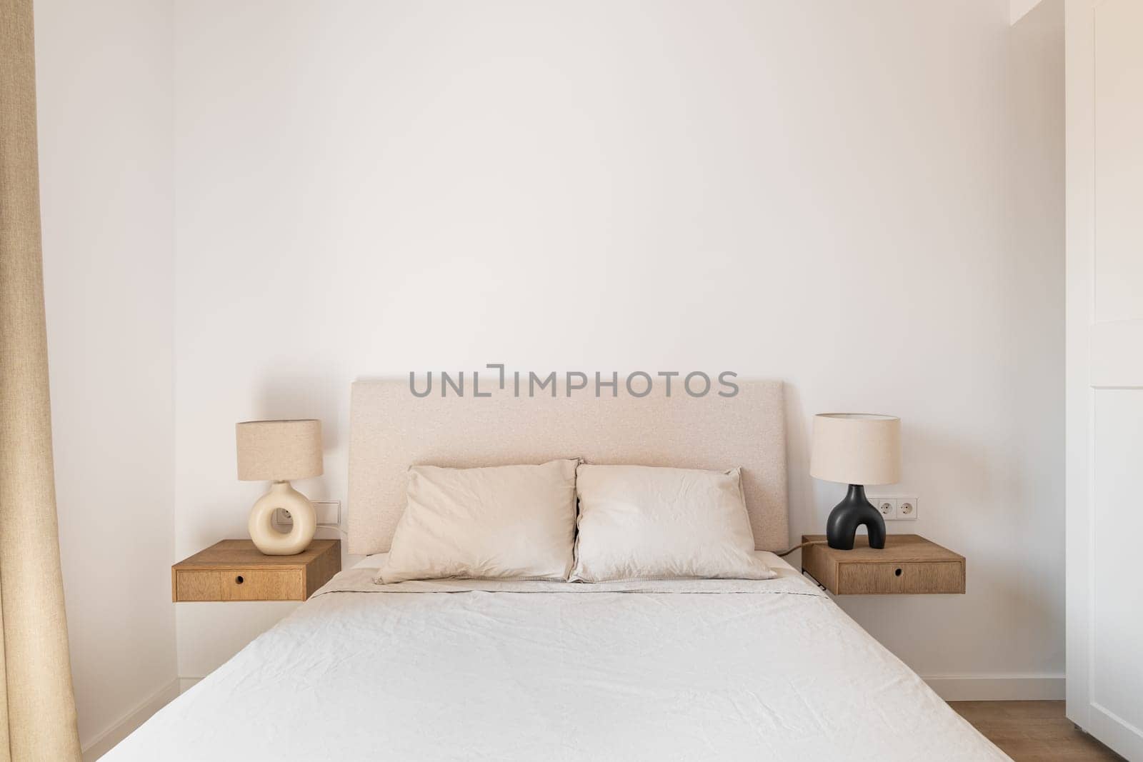 Horizontal shot of a double bed with white pillows and bedspread bedside tables sconces on a background of white wallpaper and a closet. Concept of a new apartment for a young family.