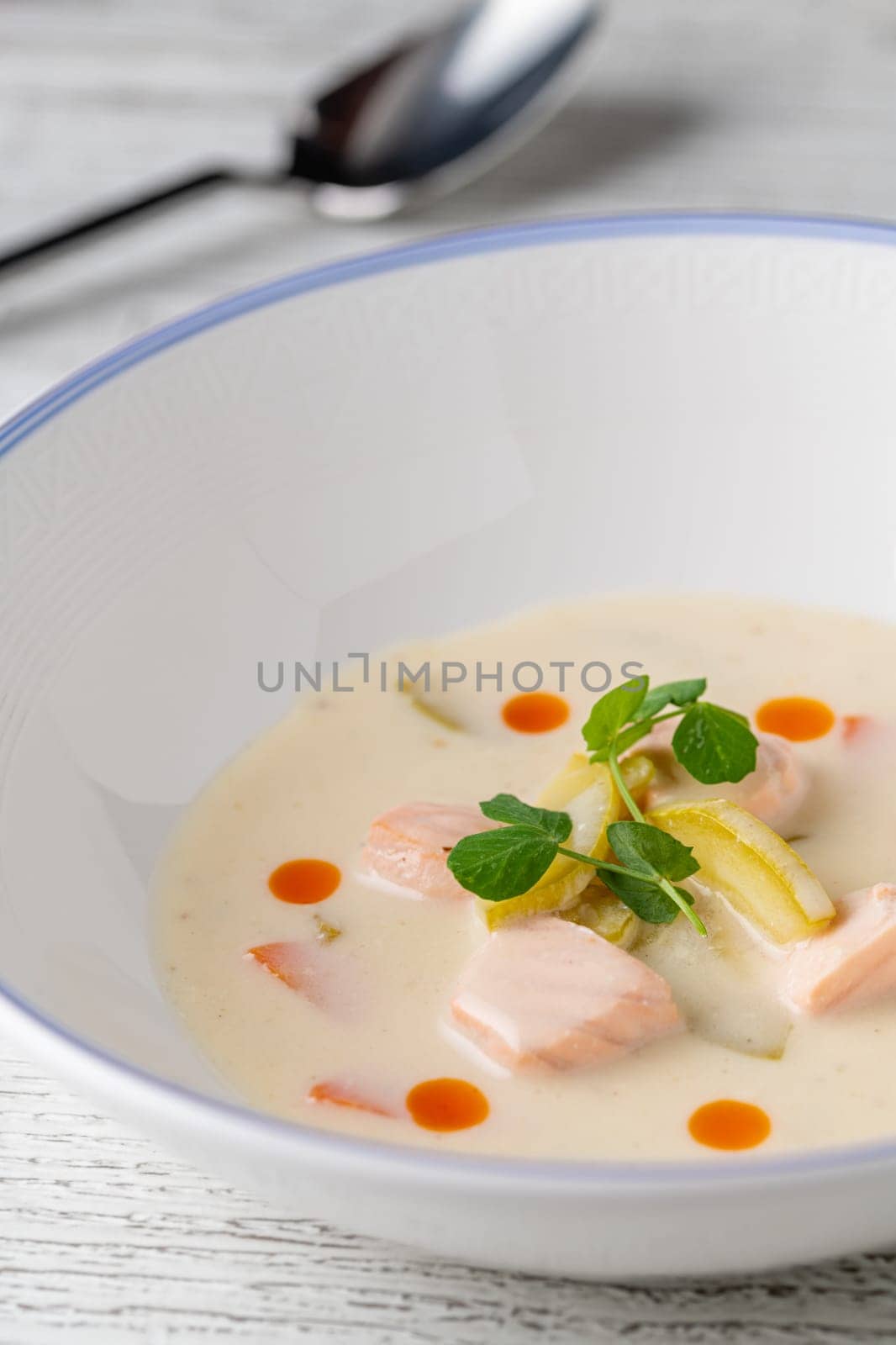Salmon soup on a white porcelain plate with salad on the side by Sonat