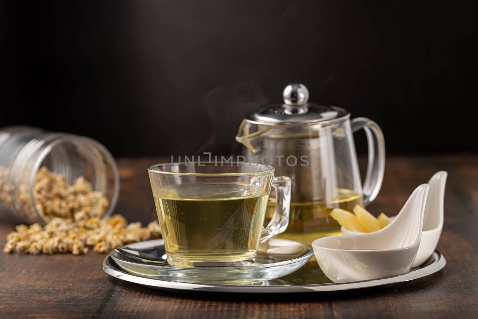 Relaxing chamomile tea in glass cup with lemon slices and honey next to it on wooden table.