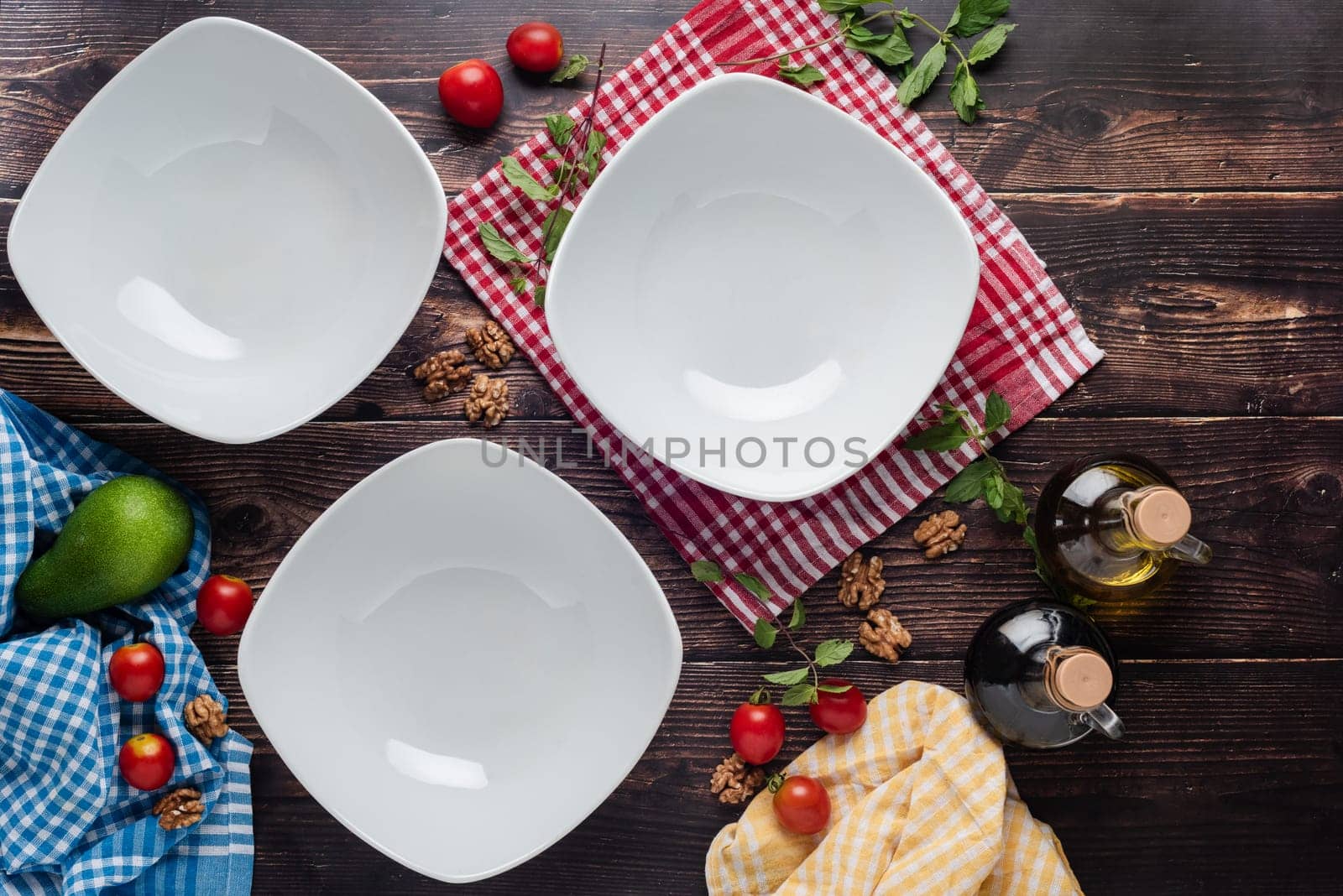 Top view of empty dinner plates with vegetables around them on wooden table