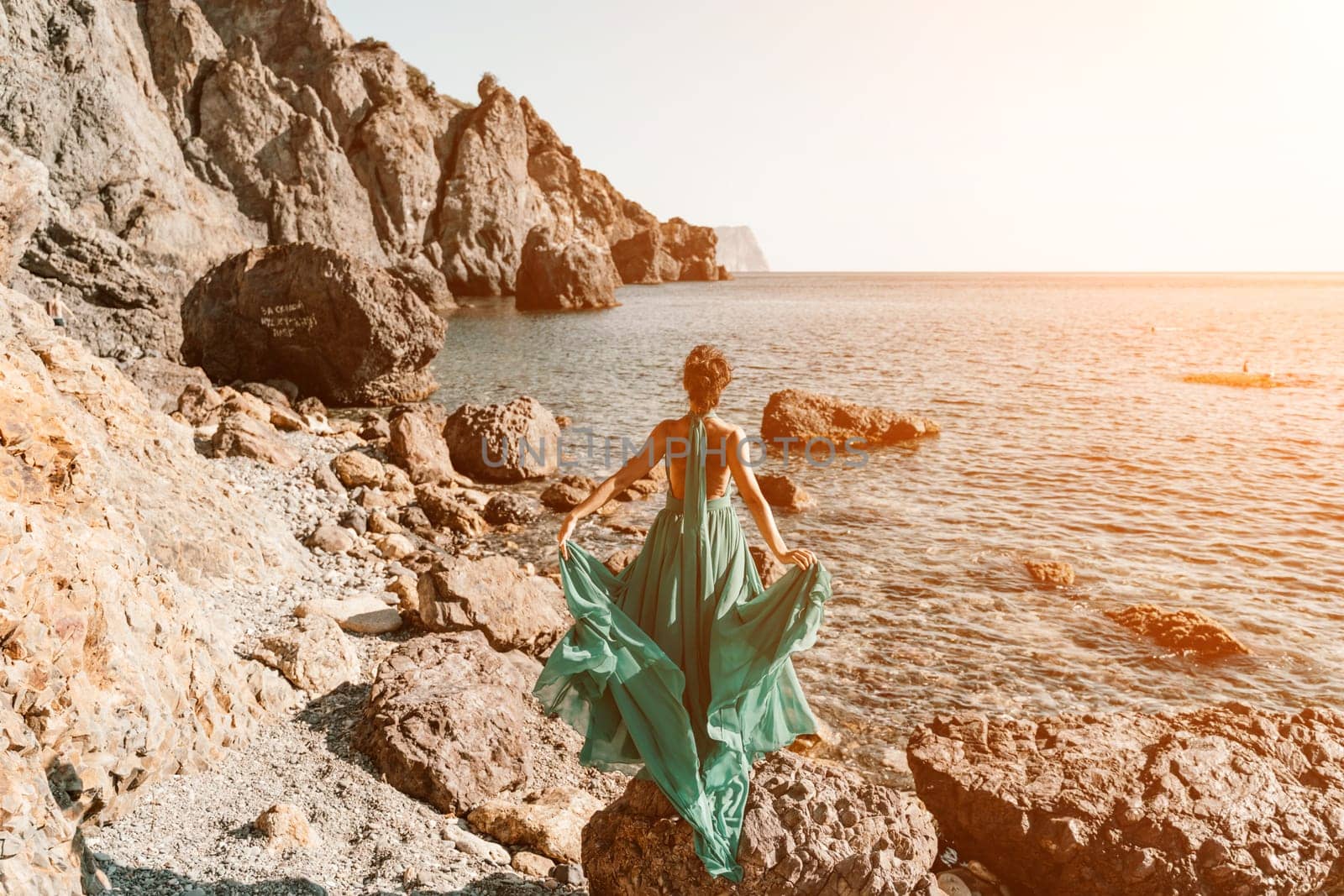 Woman green dress sea. Woman in a long mint dress posing on a beach with rocks on sunny day. Girl on the nature on blue sky background