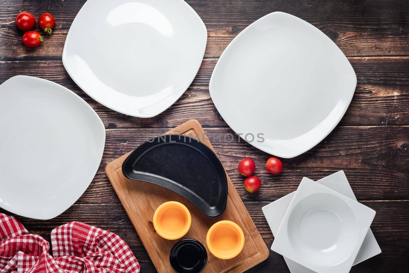 Top view of empty dinner plates with vegetables around them on wooden table