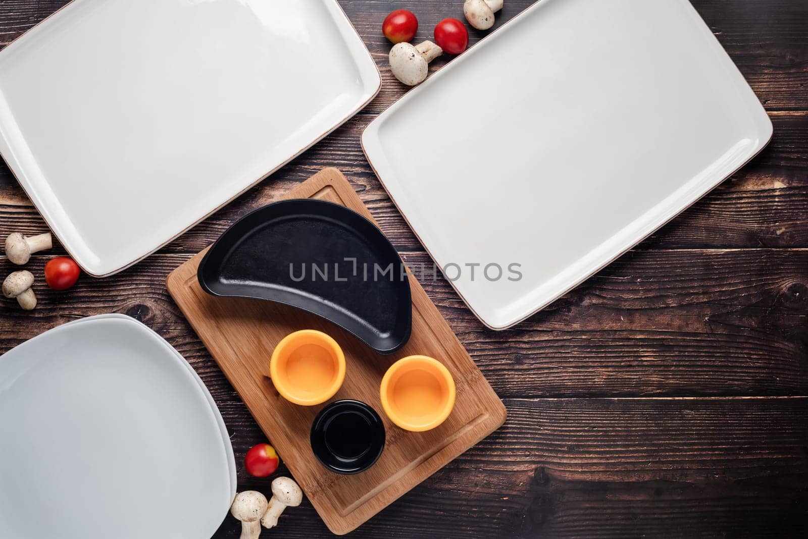 Top view of empty dinner plates with vegetables around them on wooden table