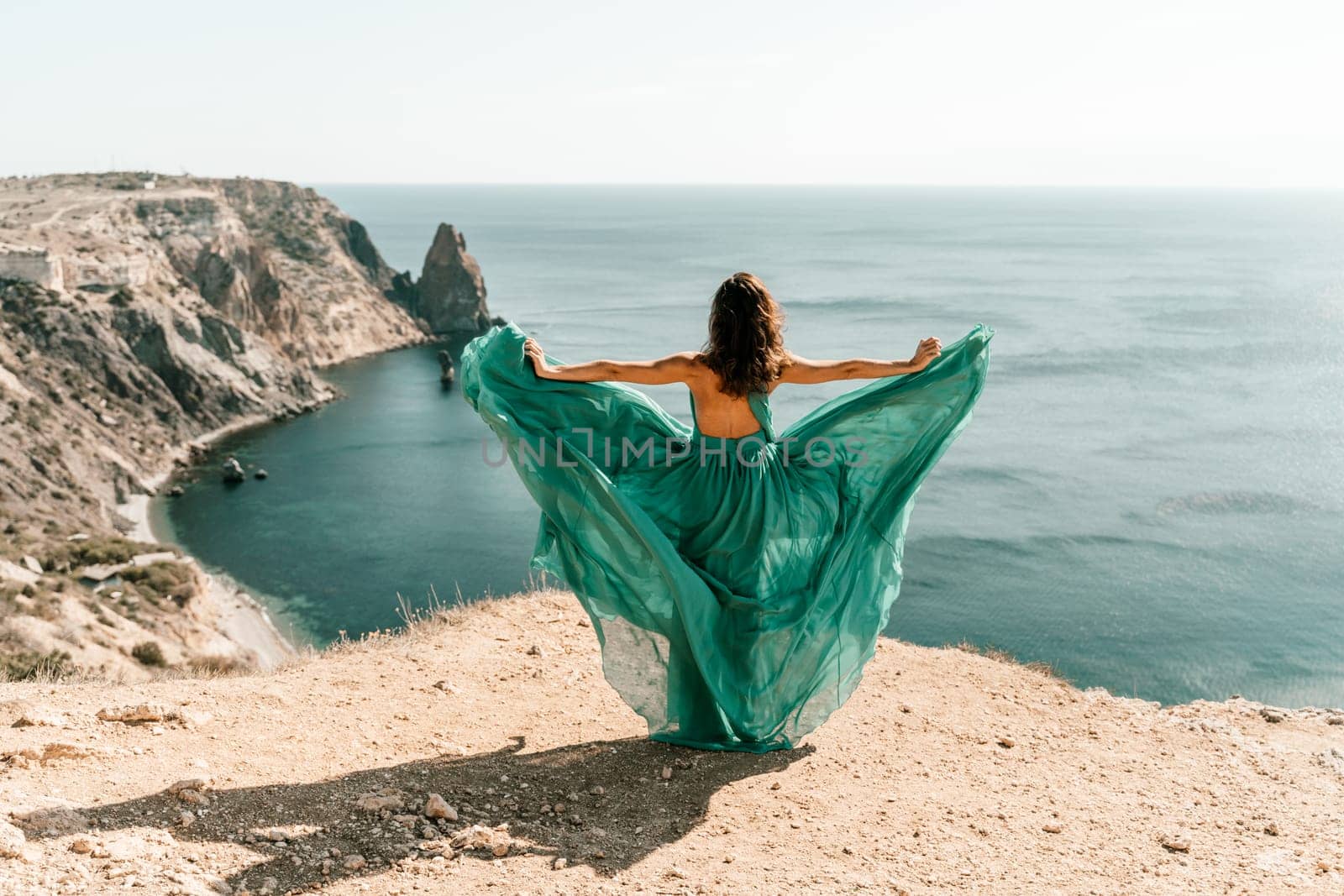 Woman green dress sea. Female dancer posing on a rocky outcrop high above the sea. Girl on the nature on blue sky background. Fashion photo. by Matiunina