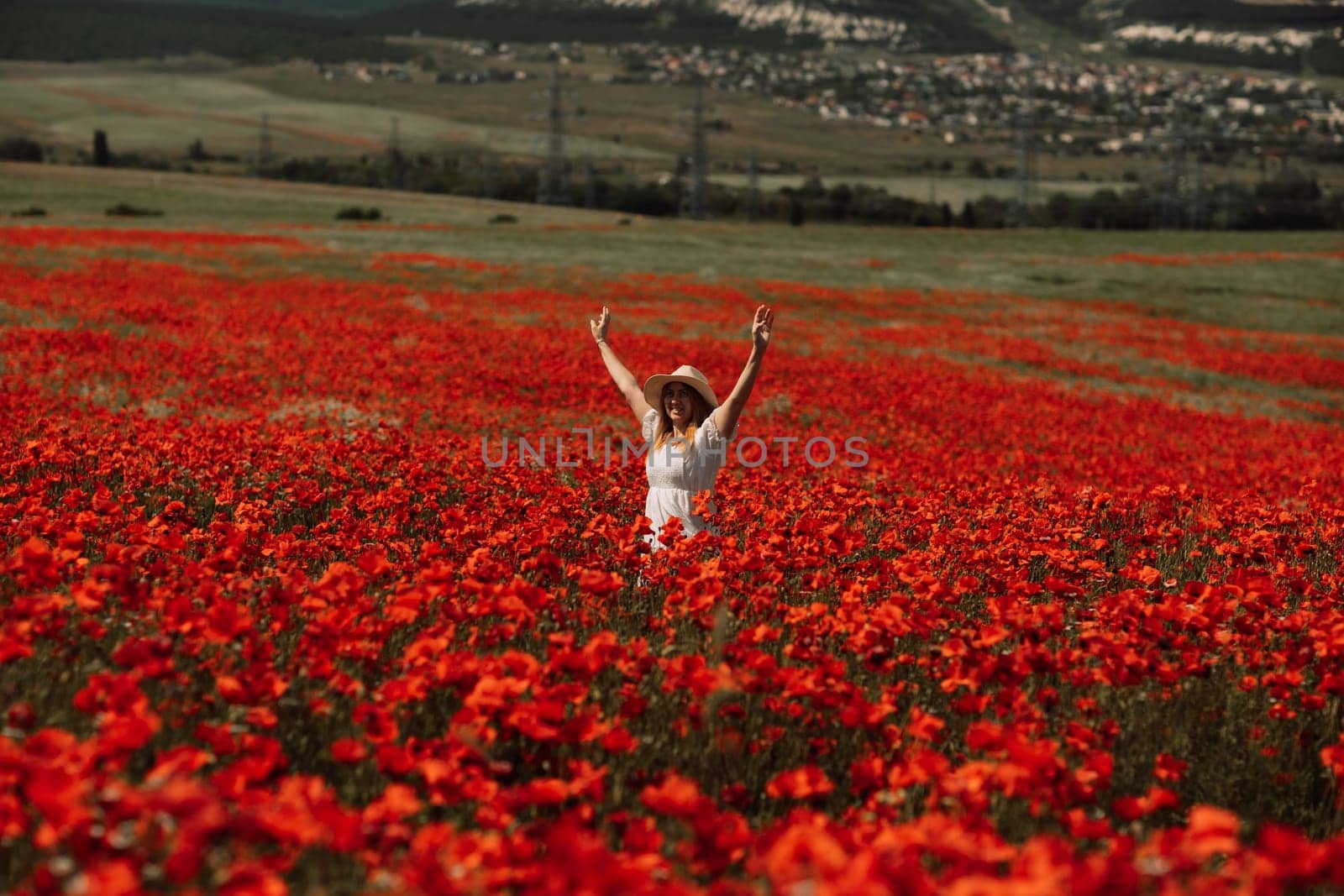 Field poppies woman. Happy woman in a white dress and hat stand through a blooming field of poppy raised her hands up. Field of blooming poppies. by Matiunina