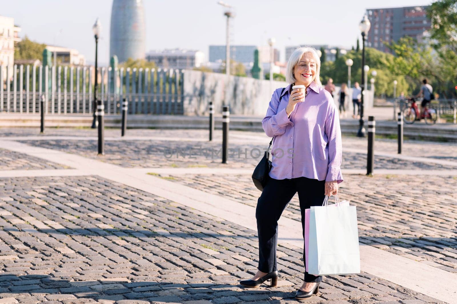 senior woman smiling standing with shopping bags and a takeaway coffee, concept of elderly people leisure and active lifestyle, copy space for text