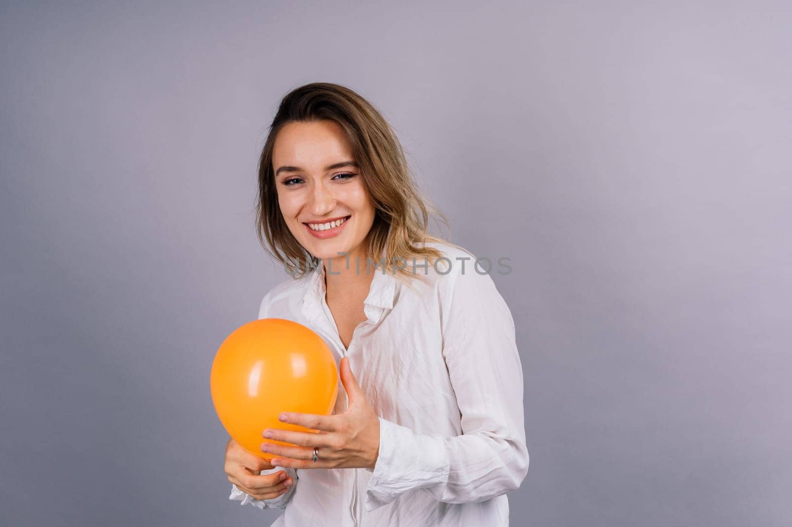 Close up portrait of young woman inflating balloon on isolated grey background