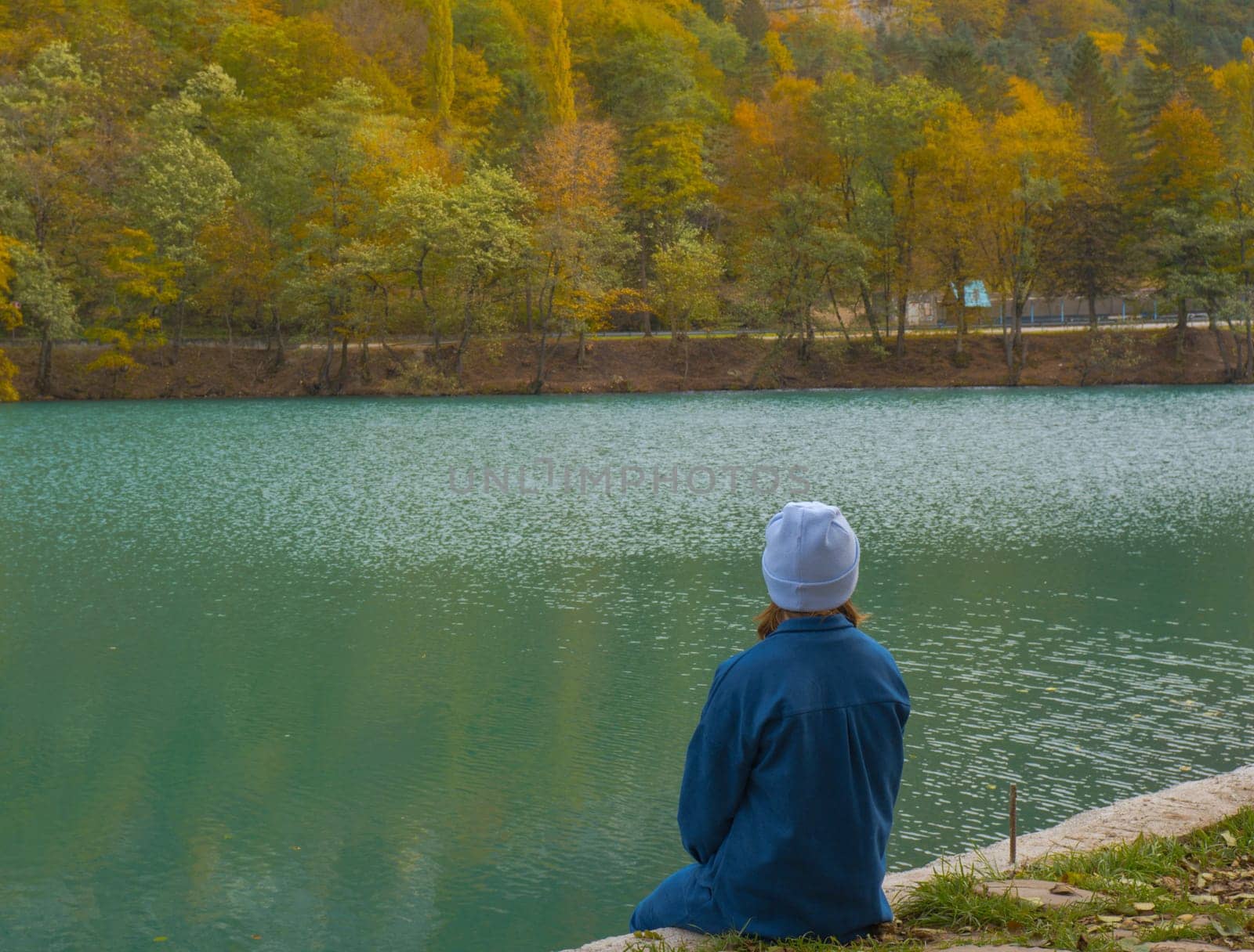 A lonely woman sits on the shore of a mountain forest lake. Autumn landscape, tranquility, tranquility, travel