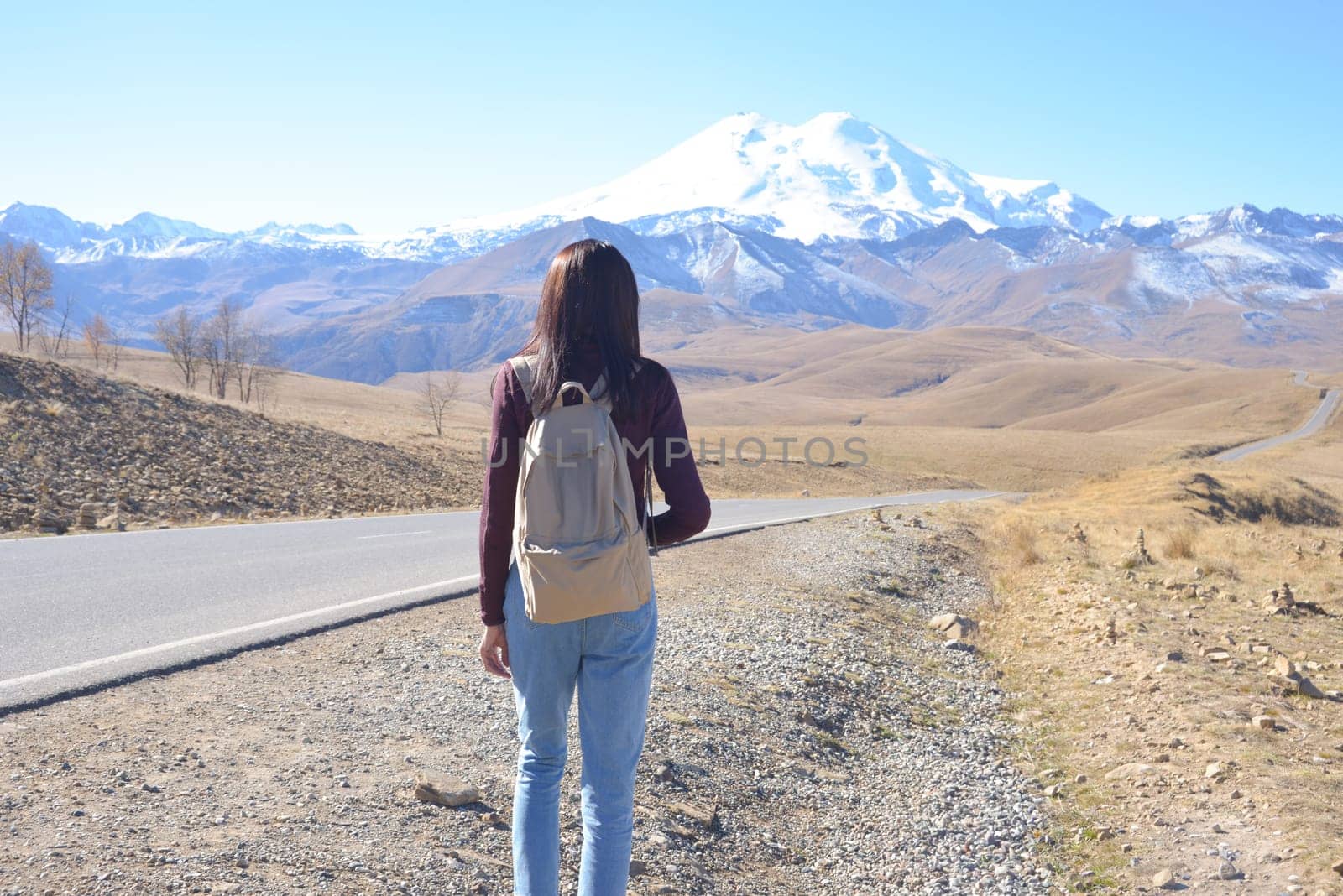 A female traveler with a backpack on her back admires the snow-covered Elbrus on a clear autumn day. View of Elbrus, North Caucasus, Russia by Ekaterina34