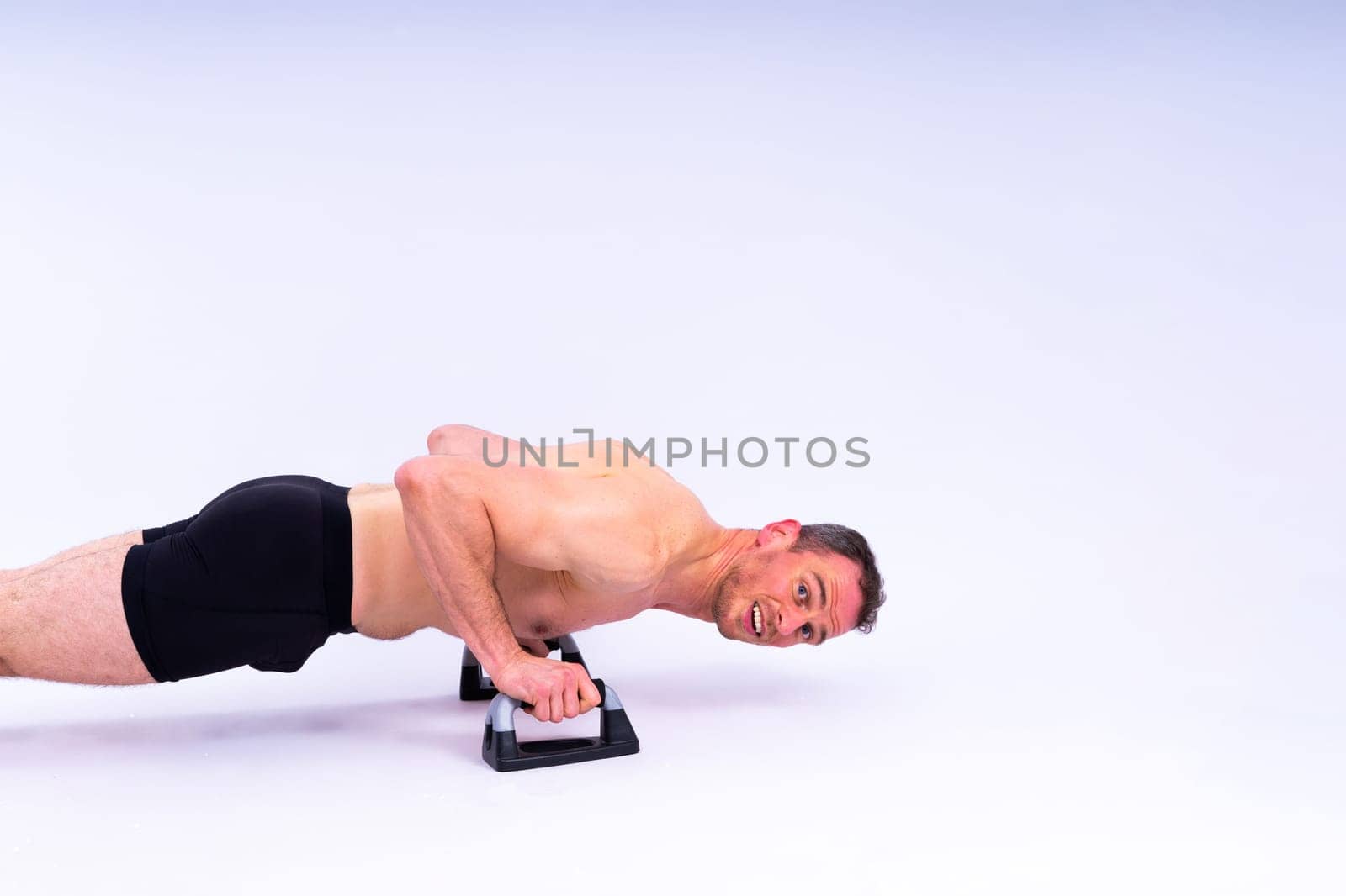 Shirtless muscular athlete do push-up on push up bars. Full body man on white studio background.