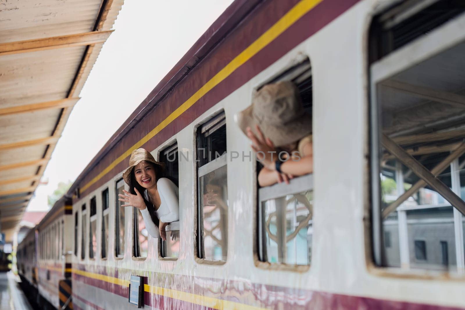 Female tourists waving at each other at train window at train station. Concept of active lifestyle and travel by itchaznong