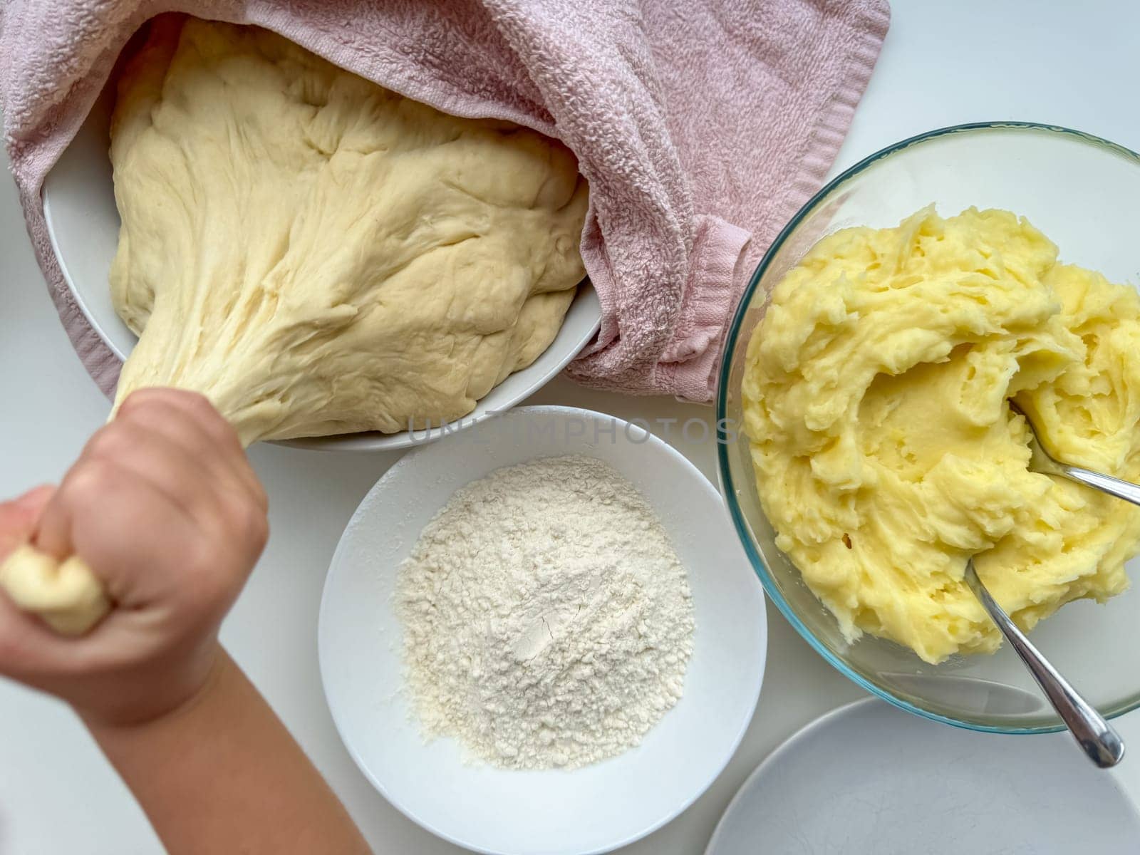 The hands of child knead the dough for making pies on white table, top view. High quality photo