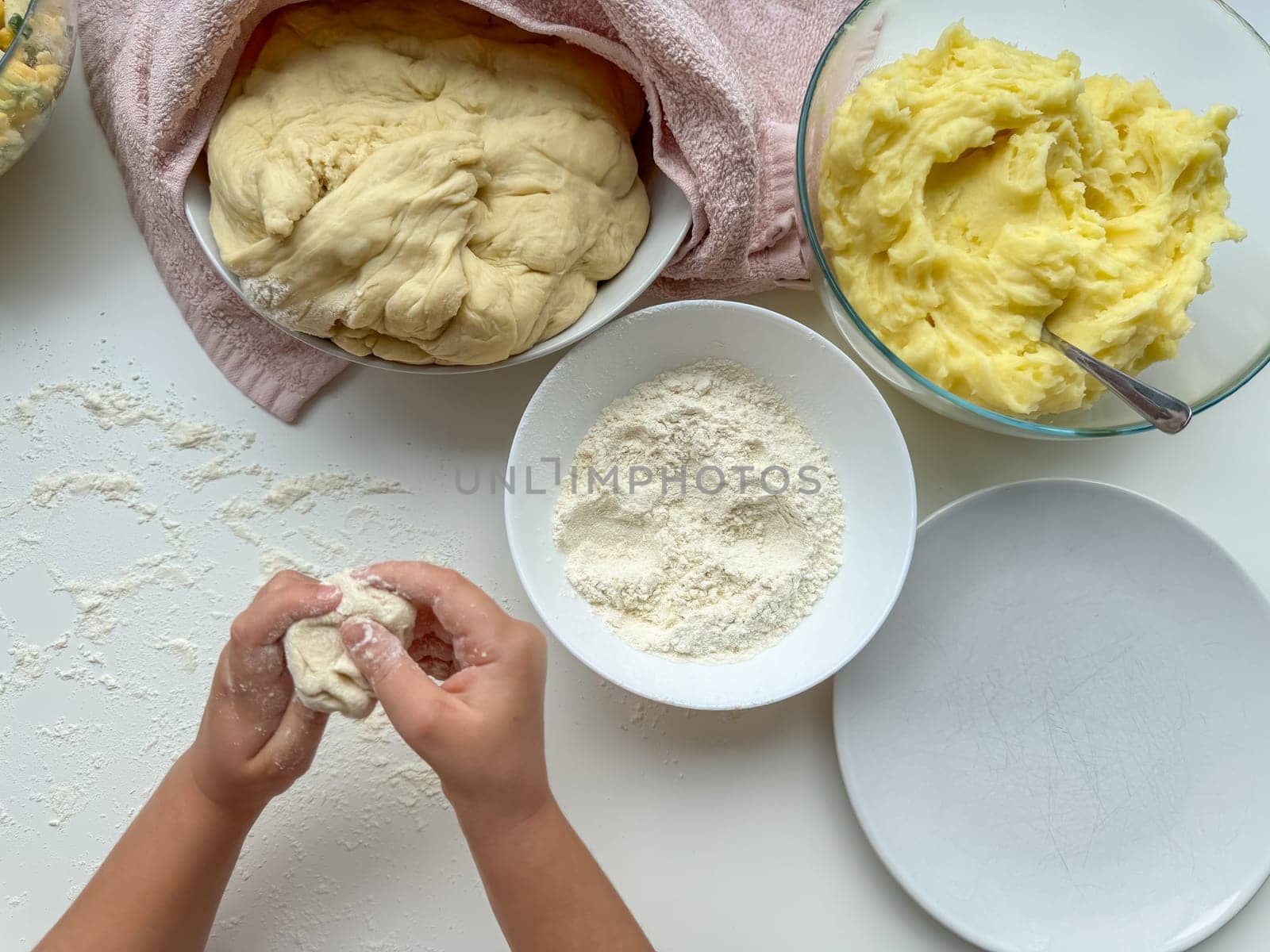 The hands of child knead the dough for making pies on white table, top view. by Lunnica