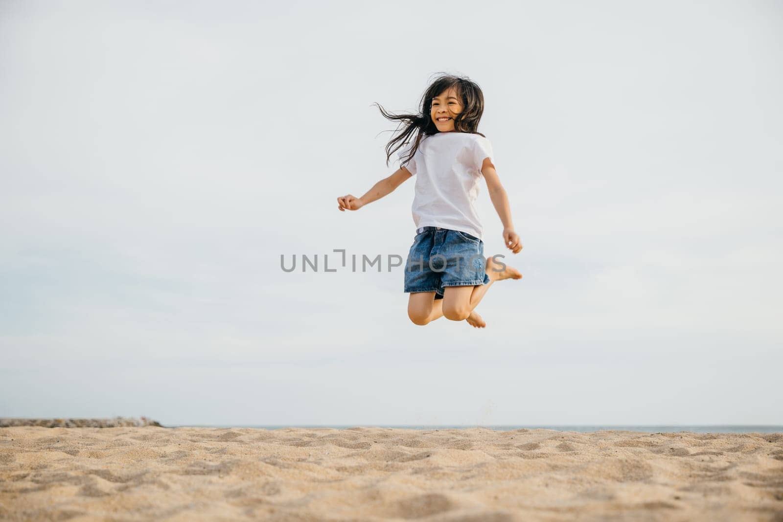 Capturing the essence of childhood a little girl jumps on the beach in the Caribbean sun. Playful motion vitality and a portrait of joy and happiness