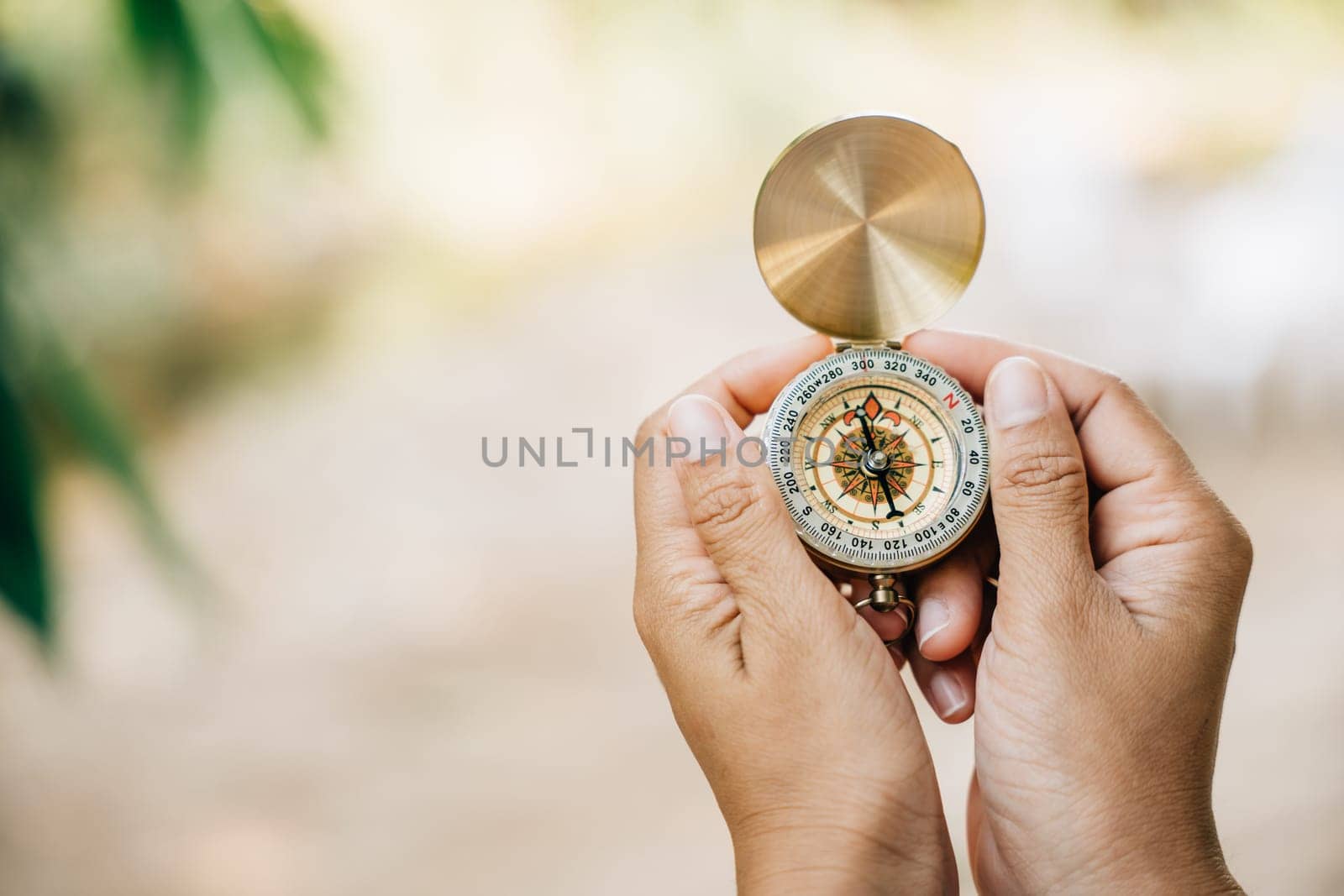 A woman's hand holds a compass in a close-up shot while hiking in the forest. The compass symbolizes guidance and exploration. by Sorapop
