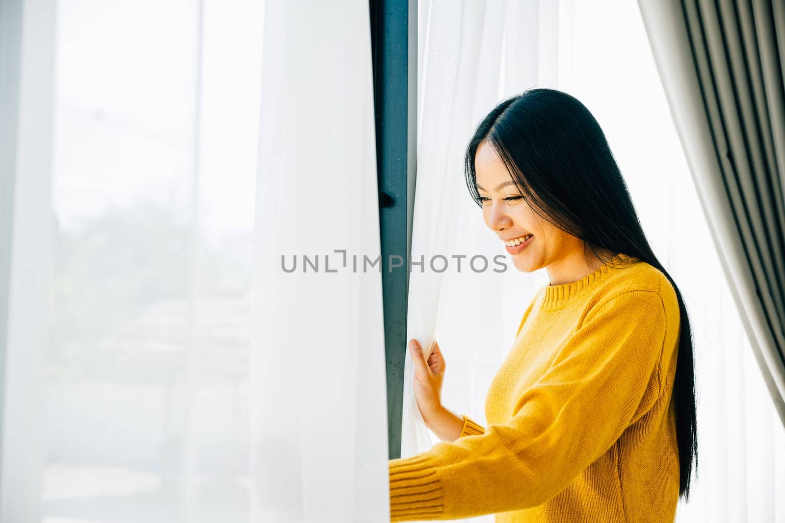 A young woman opens the curtains in the early morning smiles at the pleasant view feeling refreshed and joyful at home. Embracing morning happiness relaxation and a cheerful start.