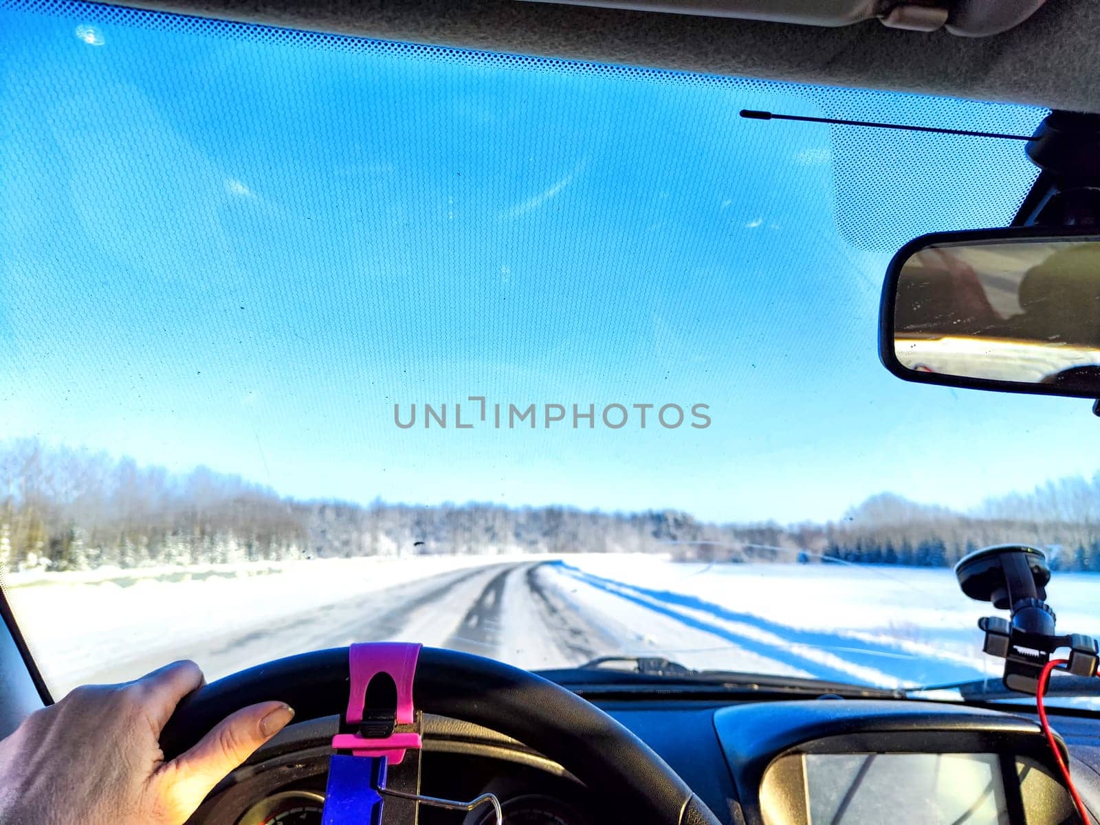 Hand of woman on the steering wheel in car and view through the windshield of a winter road with snow-covered trees