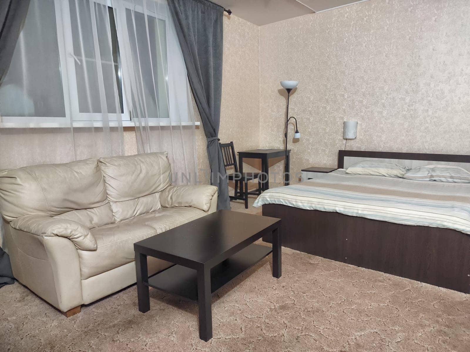Stylish bedroom in beige tones and colors with double bed, sofa, table. Concept of cozy bedroom, living room or hotel room
