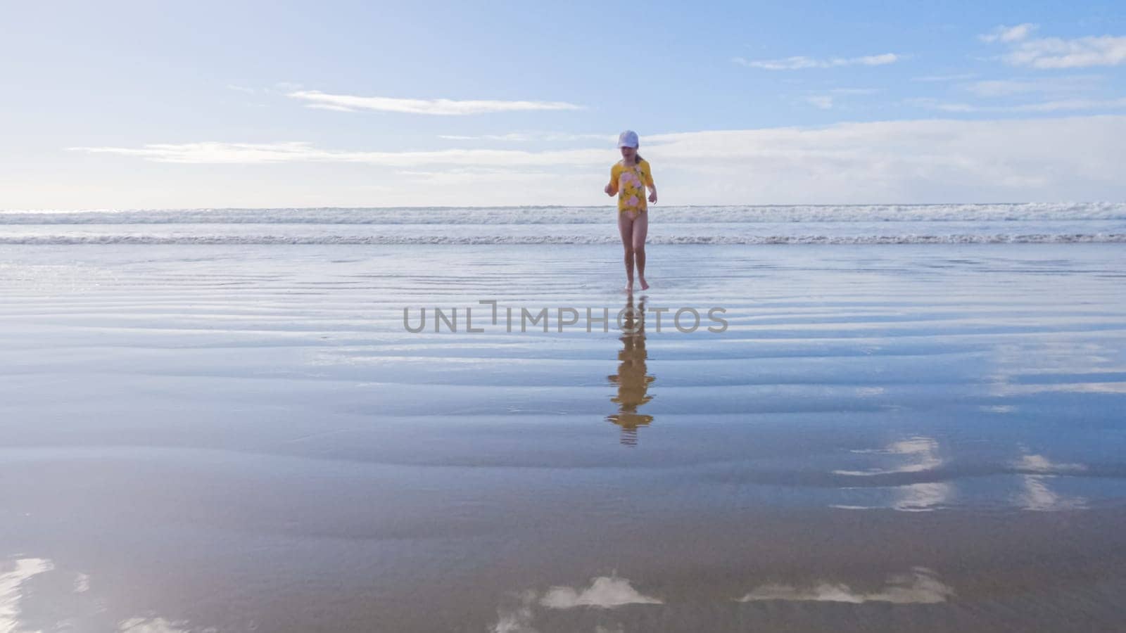 Little girl, braving the cold, joyfully runs in her swimsuit across the beach during winter.