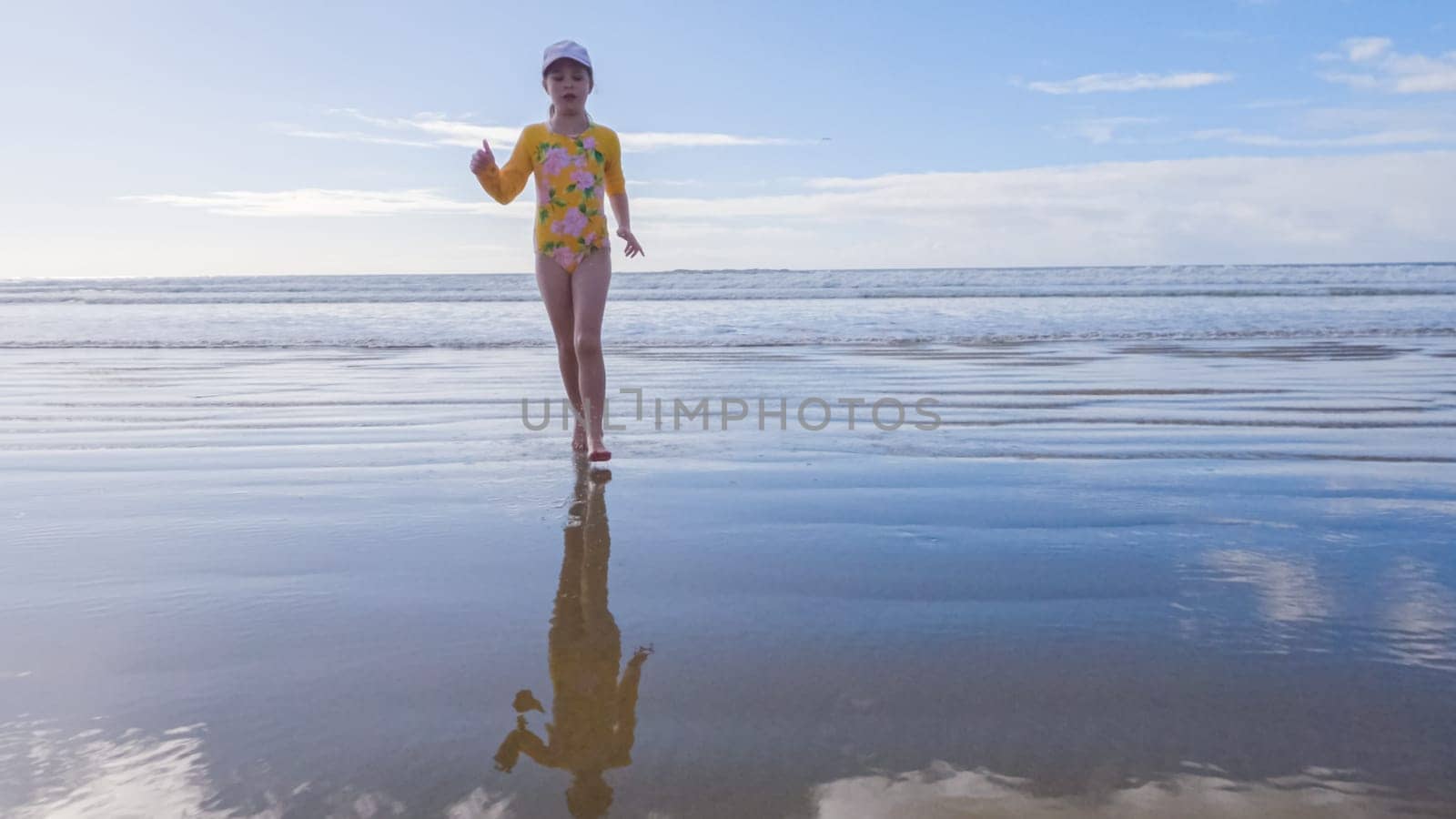 Little girl, braving the cold, joyfully runs in her swimsuit across the beach during winter.