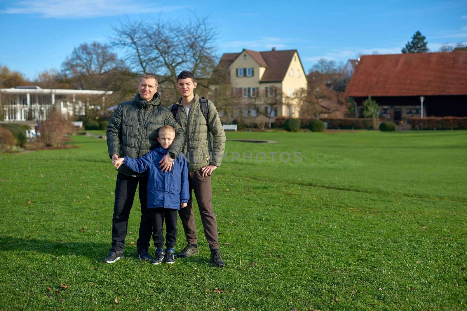 Family Harmony: Father, 40 Years Old, and Two Sons - Beautiful 8-Year-Old Boy and 17-Year-Old Young Man, Standing on the Lawn in a Park with Vintage Half-Timbered Buildings, Bietigheim-Bissingen, Germany, Autumn. Embrace the essence of family togetherness with this heartwarming image featuring a father, 40 years old, and his two sons - a beautiful 8-year-old boy and a 17-year-old young man. Standing on the lush lawn in a park with vintage half-timbered buildings in Bietigheim-Bissingen, Germany, this captures the warmth of familial bonds amidst the autumnal beauty.
