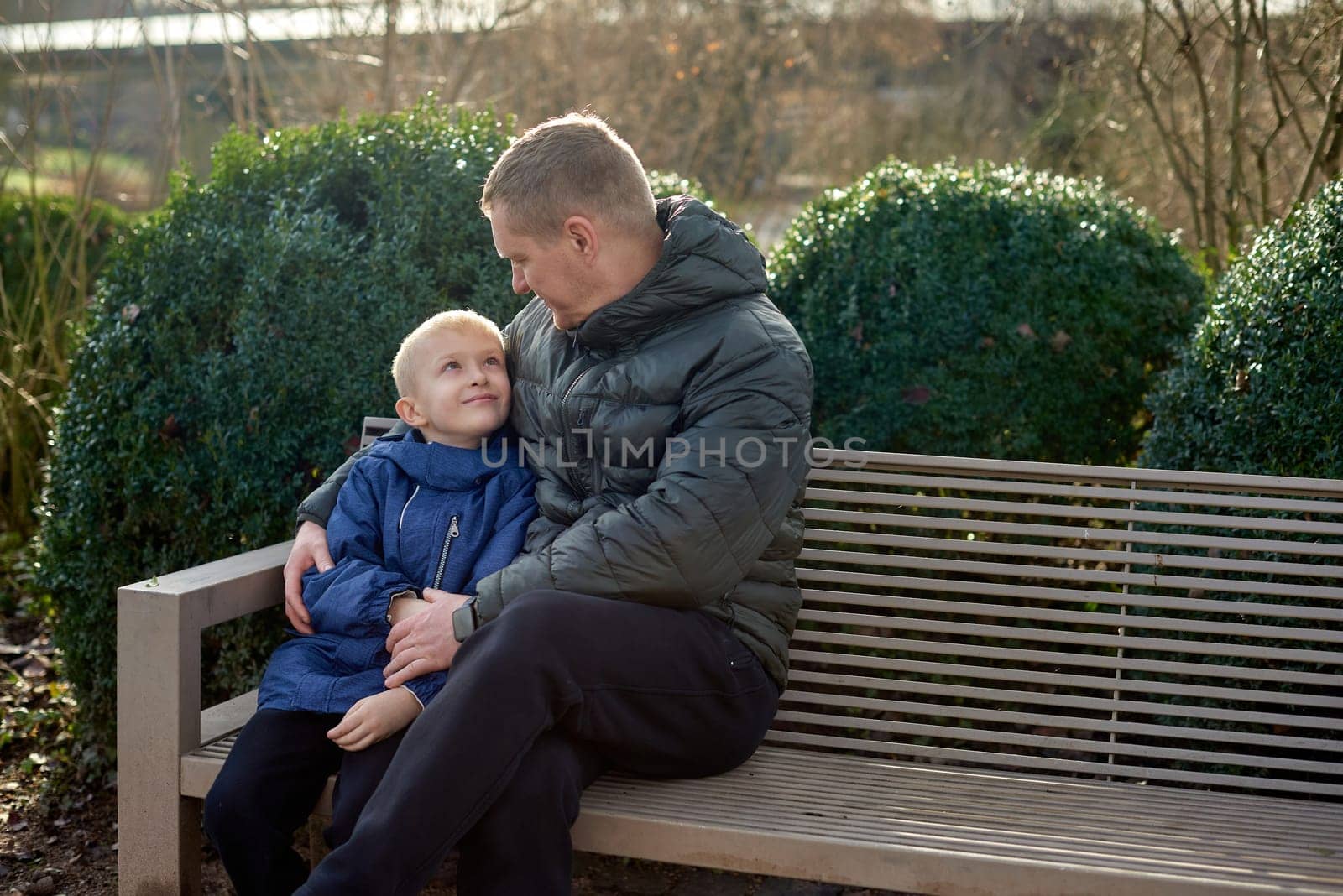 Autumnal Family Affection: Father, 40 Years Old, and Son - Beautiful 8-Year-Old Boy, Seated in the Park. Embrace the warmth of familial love in the autumnal air with this heartwarming image. A father, 40 years old, and his son - a beautiful 8-year-old boy, seated in the park. The essence of autumn adds a touch of seasonal charm to this delightful moment of family affection.