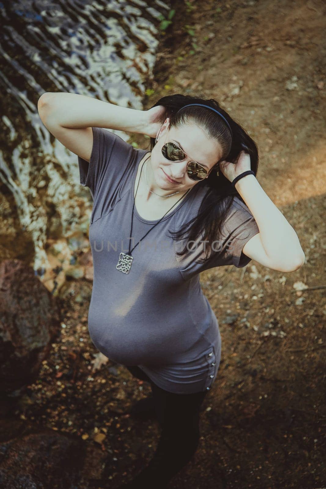 A pregnant brunette girl in mirrored sunglasses stands in a park near the waters, a close-up view from above