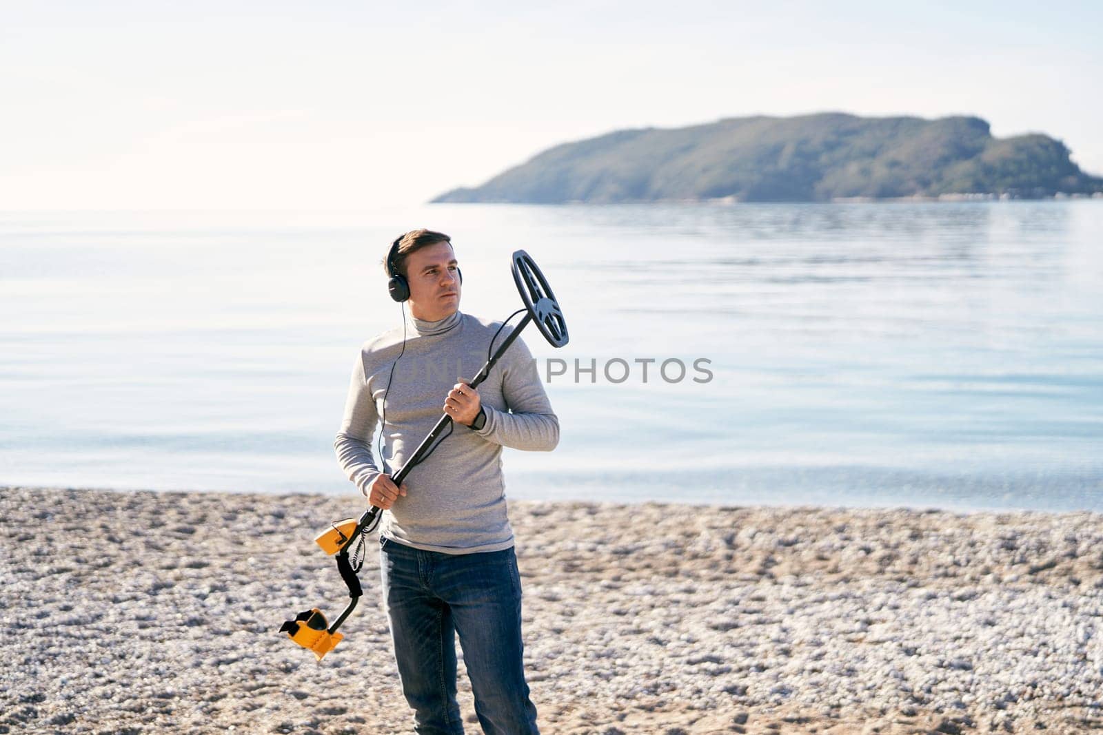 Young man stands on the seashore holding up a metal detector. High quality photo