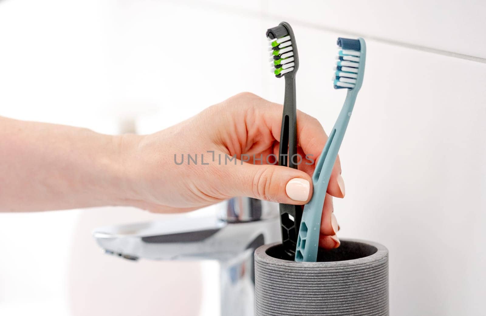 Girl'S Hand Places Two Toothbrushes In Cup For Hygiene In Bright Bathroom