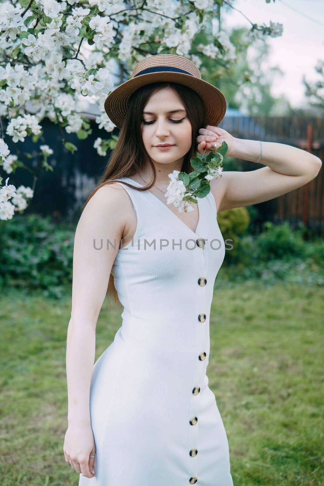 Beautiful young girl in white dress and hat in blooming Apple orchard. Blooming Apple trees with white flowers