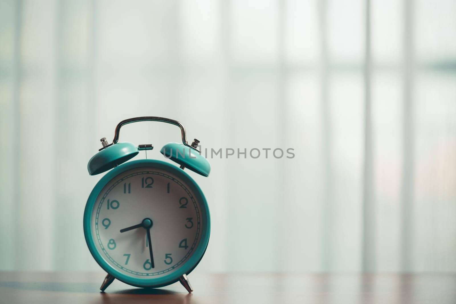 Table with a vintage alarm clock, set against the curtains with morning sunlight shining on, showcasing a classic metal timepiece with retro charm and a sense of urgency