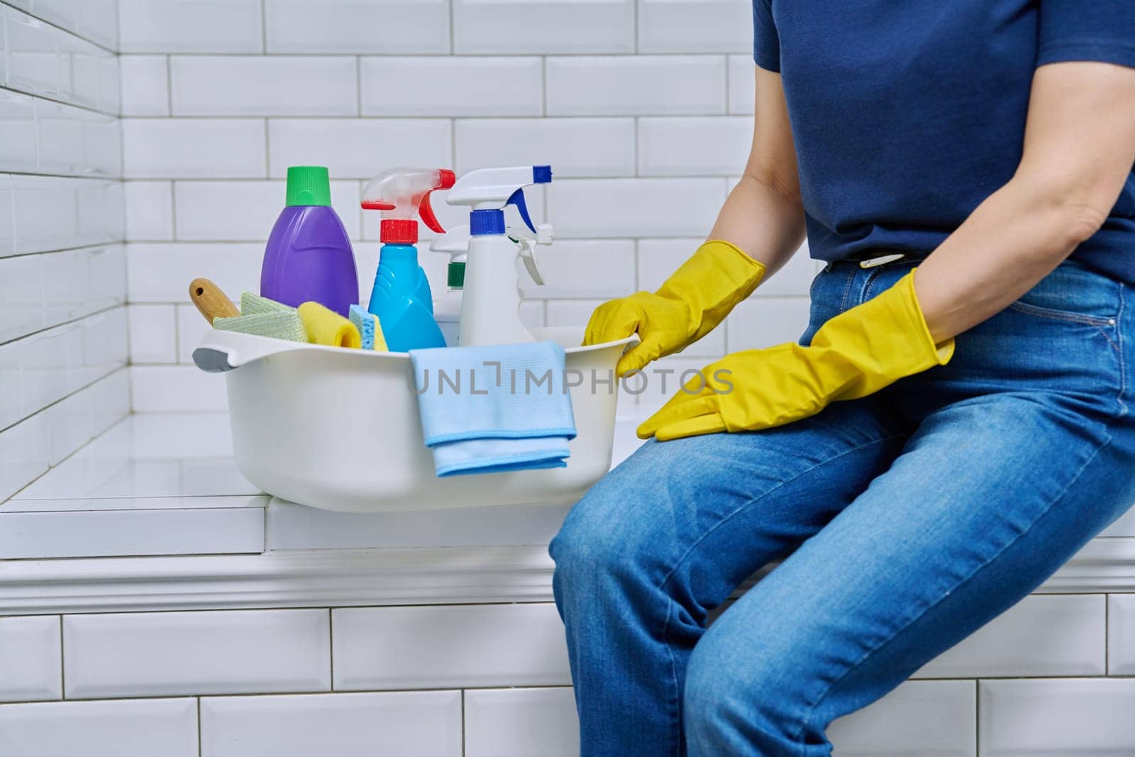 House cleaning housework concept, housekeeping housecleaning service, close-up of basin with cleaning products and washcloths, brushes, rags and woman hands in rubber protective gloves, in bathroom