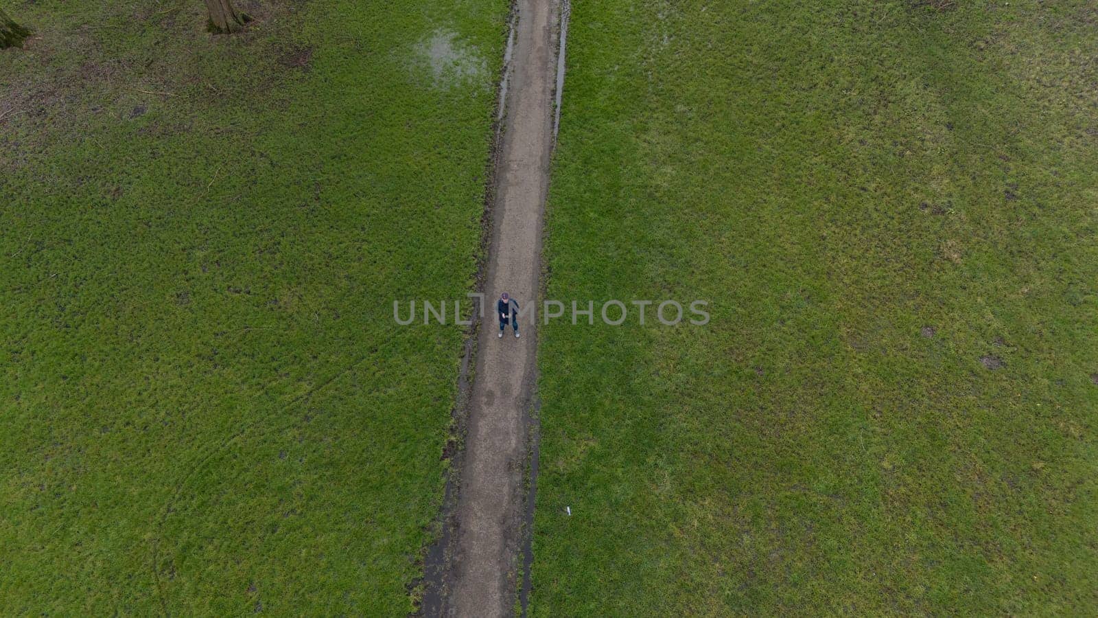 Aerial view of man flying a drone or UAV , standing on a trqack in a green field with grass