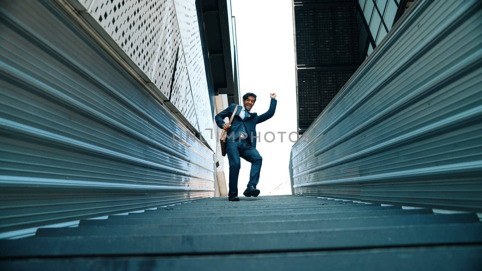Low angle view of young smiling business man dance between building at center point. Skilled executive manager wearing suit and suitcase and moving to music. Happy investor moving to music. Exultant.