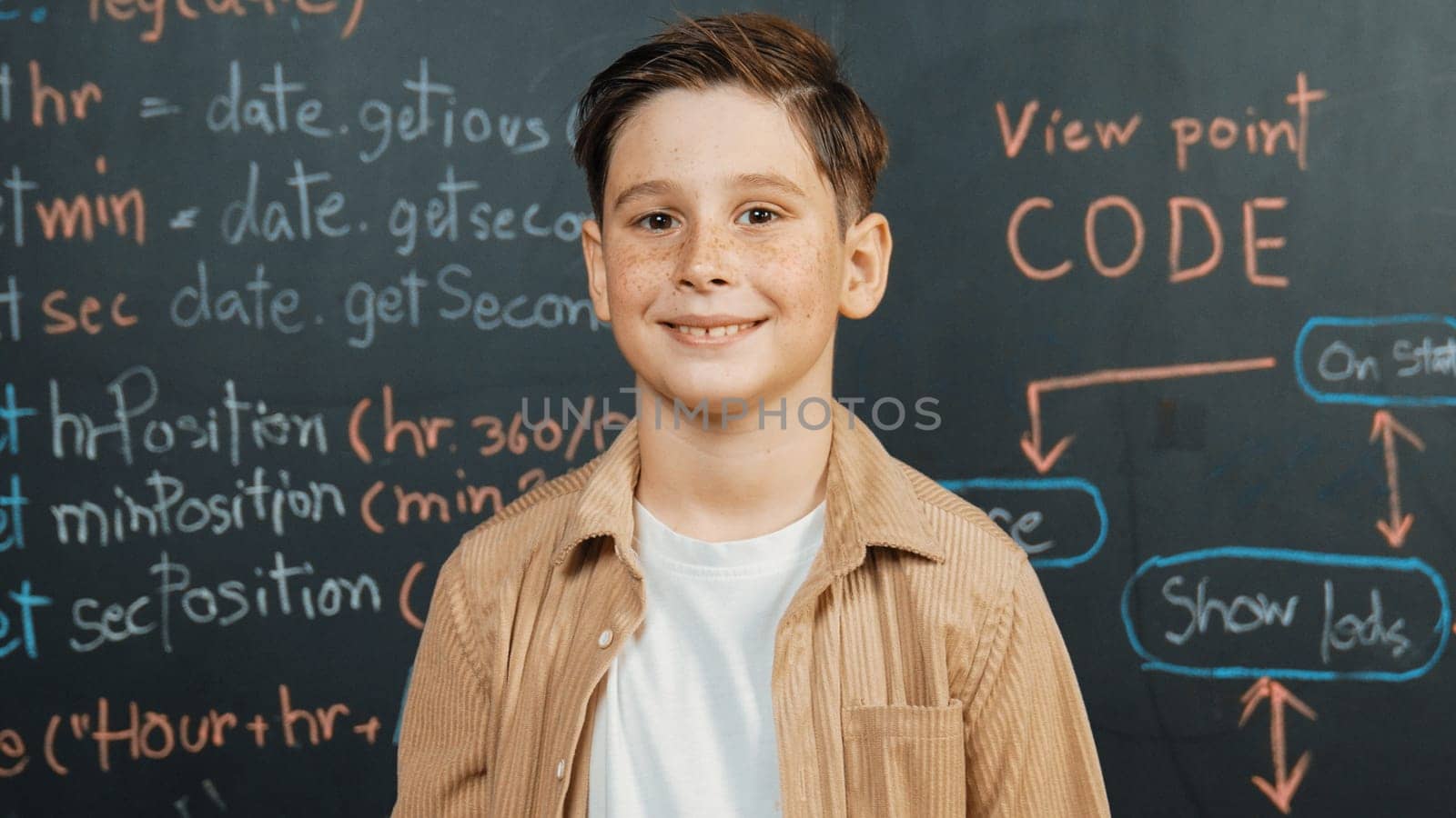 Panorama shot of happy caucasian boy smiling and standing at blackboard with engineering code or prompt written. Smart child looking at camera and greeting while study in STEM classroom. Erudition.