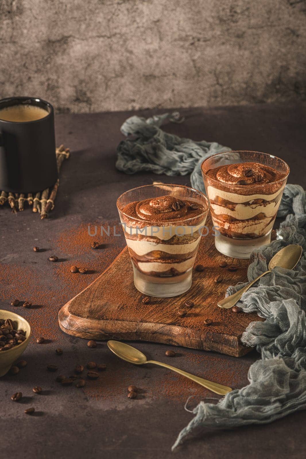 Delicious italian dessert tiramisu in a glasses on a dark slate, stone or concrete background.