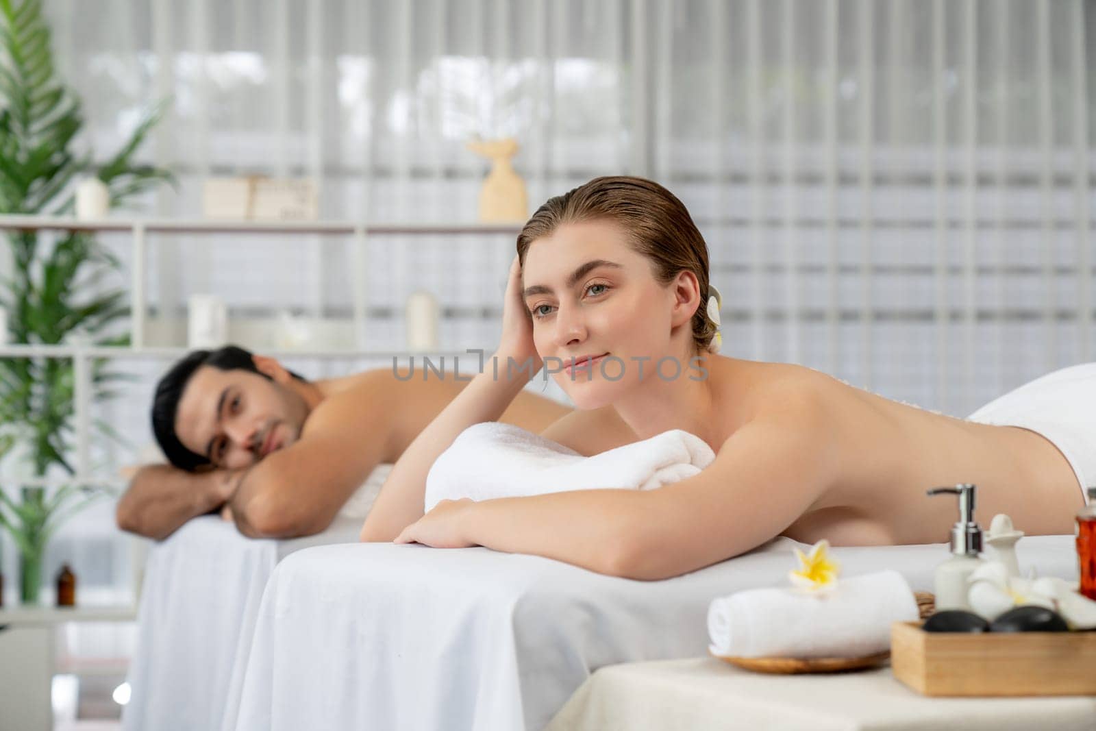 Blissful couple customer having exfoliation treatment in luxury spa salon with warmth candle light ambient. Salt scrub beauty treatment in health spa body scrub. Quiescent