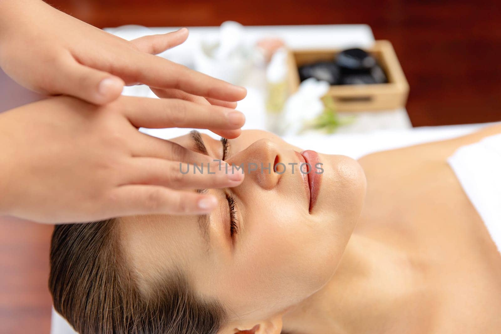 Closeup woman enjoying relaxing anti-stress head massage and pampering facial beauty skin recreation leisure in dayspa modern light ambient at luxury resort or hotel spa salon. Quiescent
