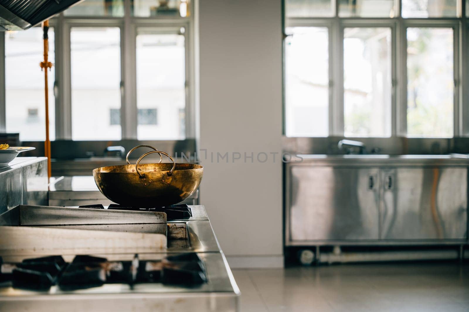 A shiny metal bowl adorns the stove in a professional kitchen of a modern restaurant. Clean arrangement of chrome appliances equipment and new furniture. Bright gas service is working.