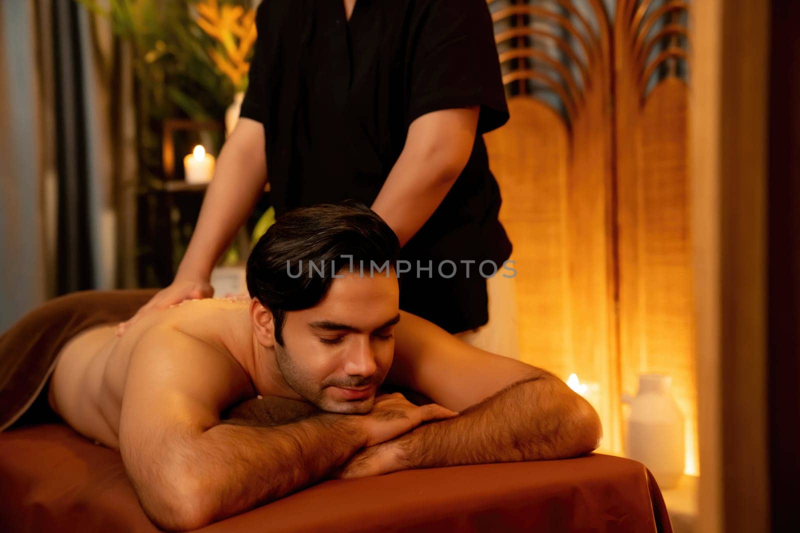 Man customer having exfoliation treatment in luxury spa salon with warmth candle light ambient. Salt scrub beauty treatment in Health spa body scrub. Quiescent