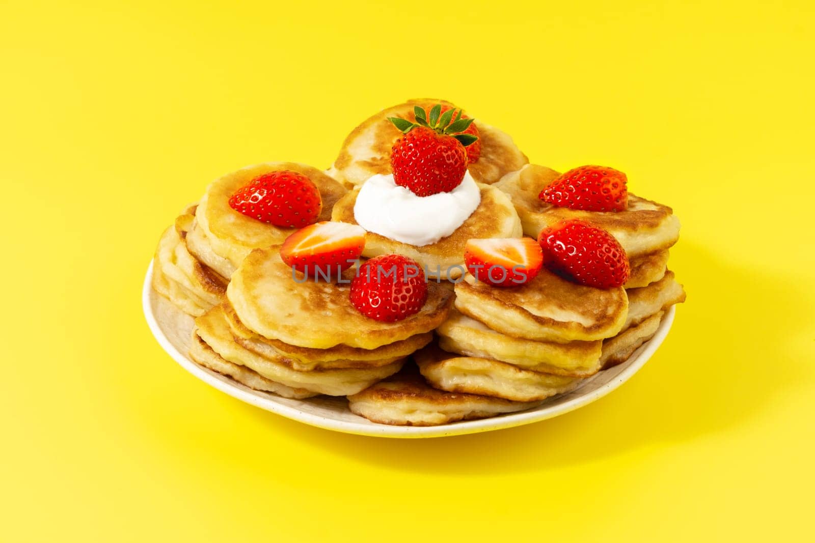 Mini pancakes with strawberries and sour cream on a yellow background.